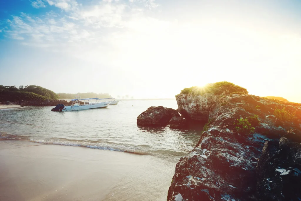 Small boats anchored in the calm waters of Akumal Bay next to rocky shores at sunrise